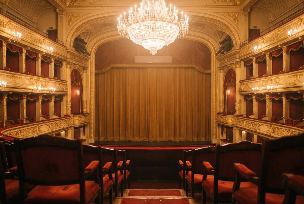 Sala di un teatro storico con palchi dorati e lampadario acceso
