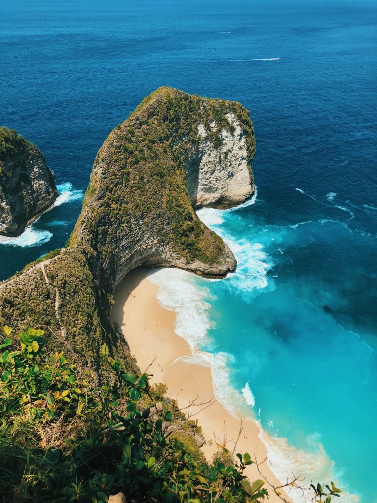 Scogliera verde a picco su una spiaggia bianca e mare turchese, meta tropicale fuori dai circuiti di massa